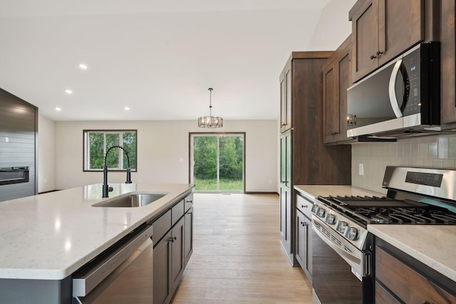 kitchen featuring sink, stainless steel appliances, a chandelier, decorative light fixtures, and a center island with sink