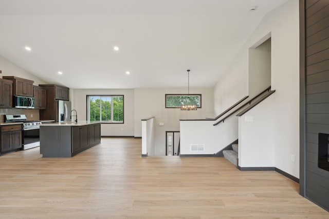 kitchen with an island with sink, decorative light fixtures, light hardwood / wood-style floors, dark brown cabinets, and stainless steel appliances