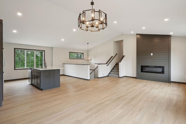 kitchen featuring sink, a center island with sink, light hardwood / wood-style flooring, a fireplace, and hanging light fixtures