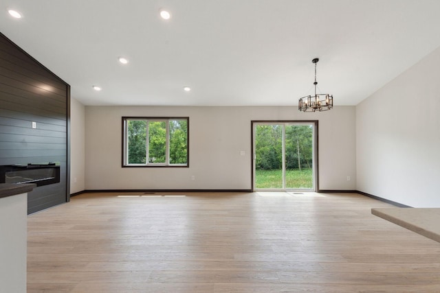 unfurnished living room featuring vaulted ceiling, light wood-type flooring, and a chandelier