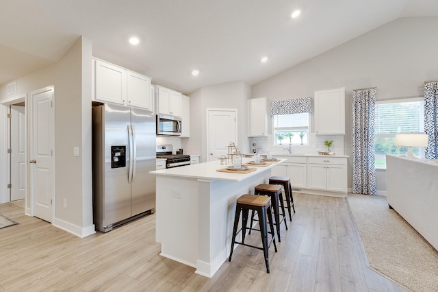 5181 Mustang Ct, Woodbury, MN 55129 - kitchen with appliances with stainless steel finishes, vaulted ceiling, a kitchen island with sink, a breakfast bar area, and white cabinetry