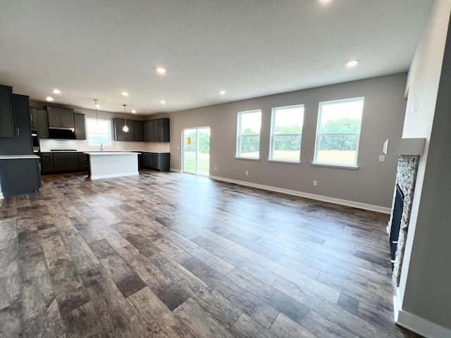 unfurnished living room featuring dark hardwood / wood-style floors, sink, a stone fireplace, and a textured ceiling