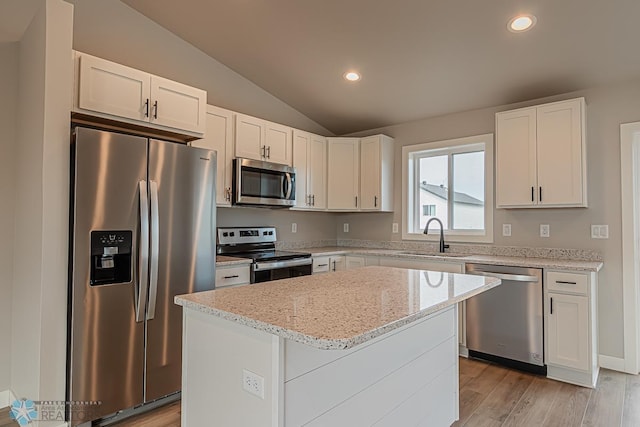 kitchen with light stone countertops, appliances with stainless steel finishes, sink, white cabinets, and a kitchen island