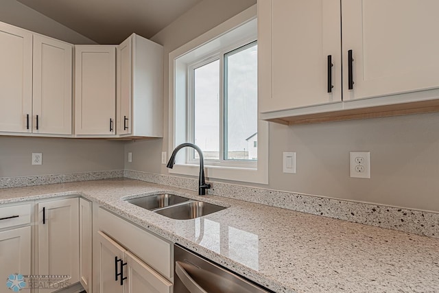 kitchen featuring lofted ceiling, sink, stainless steel dishwasher, light stone counters, and white cabinetry