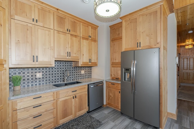 kitchen featuring light stone countertops, light brown cabinetry, decorative backsplash, a sink, and appliances with stainless steel finishes