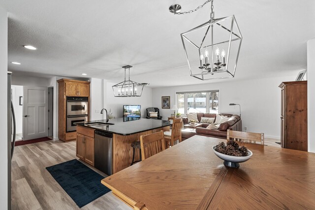 kitchen featuring decorative light fixtures, light wood-type flooring, a notable chandelier, stainless steel appliances, and a kitchen island with sink