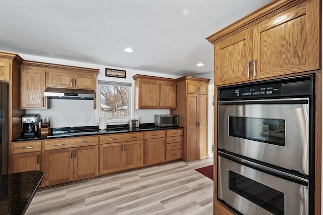 kitchen with appliances with stainless steel finishes, light wood-type flooring, and dark stone counters