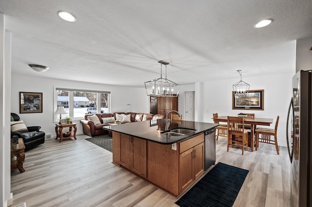 kitchen featuring sink, hanging light fixtures, fridge, stainless steel dishwasher, and a center island with sink