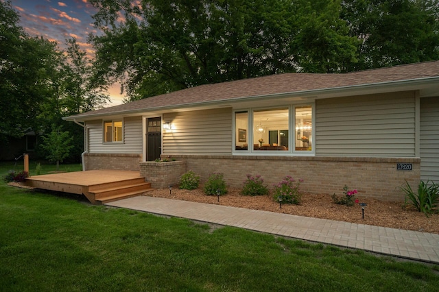 back house at dusk with a wooden deck and a lawn