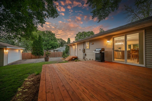 deck at dusk with a garage, grilling area, and a lawn