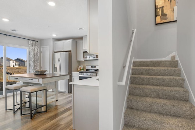 kitchen with white cabinetry, stainless steel appliances, a kitchen breakfast bar, decorative backsplash, and light wood-type flooring