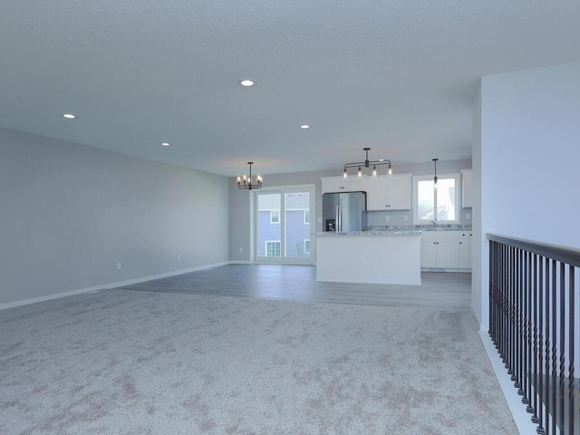 unfurnished living room with light colored carpet, sink, and an inviting chandelier