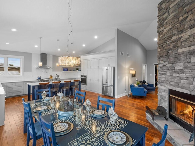 dining area with light hardwood / wood-style flooring, a stone fireplace, and lofted ceiling