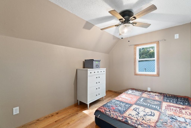 bedroom with a textured ceiling, ceiling fan, vaulted ceiling, and light wood-type flooring