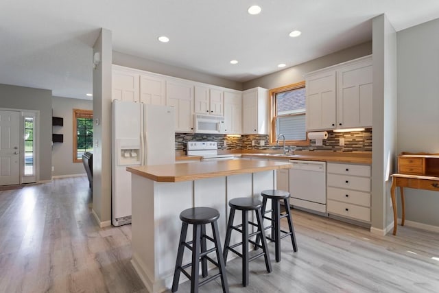 kitchen with a center island, a kitchen breakfast bar, tasteful backsplash, white appliances, and white cabinets