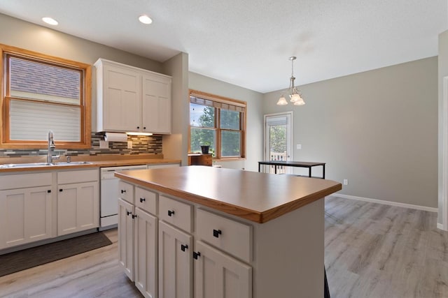 kitchen featuring pendant lighting, a center island, white dishwasher, white cabinets, and sink