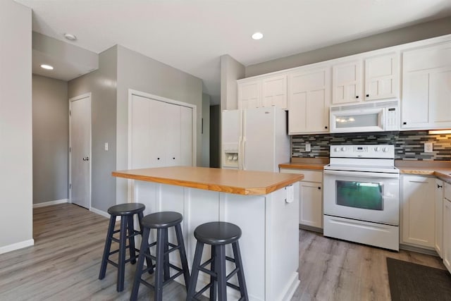 kitchen with a center island, white appliances, a breakfast bar area, decorative backsplash, and white cabinets