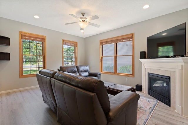 living room with light wood-type flooring, ceiling fan, and a tiled fireplace