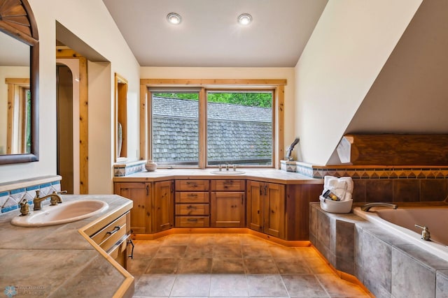 bathroom featuring tiled tub, vanity, and vaulted ceiling