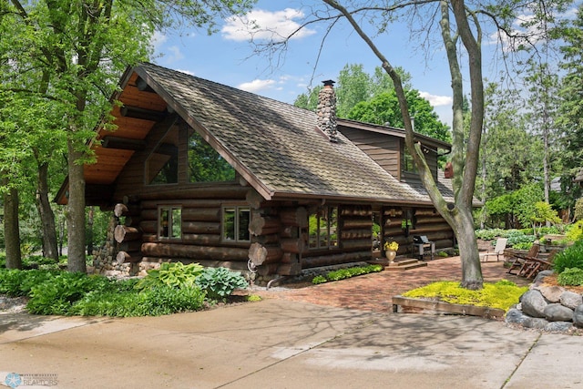 view of front facade featuring log siding, a patio area, and a chimney