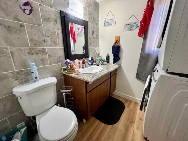 bathroom with stacked washer and dryer, toilet, wood-type flooring, tile walls, and vanity