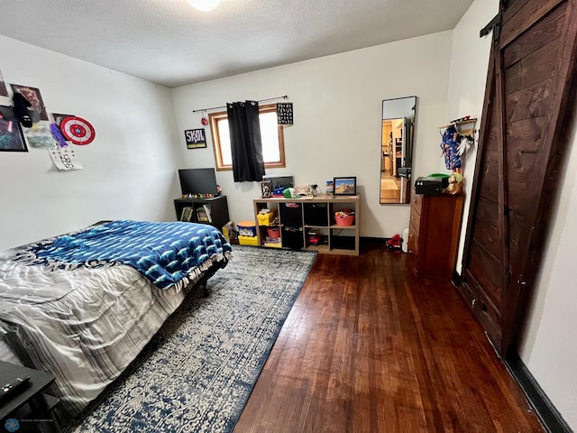 bedroom featuring dark hardwood / wood-style flooring, a barn door, and a textured ceiling