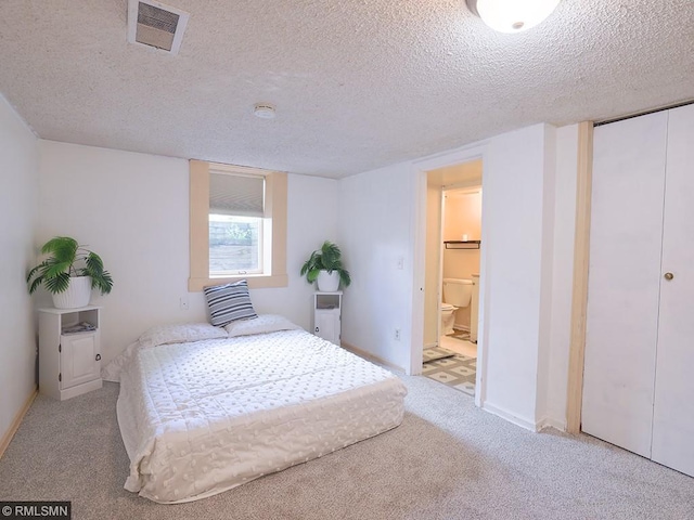 carpeted bedroom with ensuite bathroom and a textured ceiling