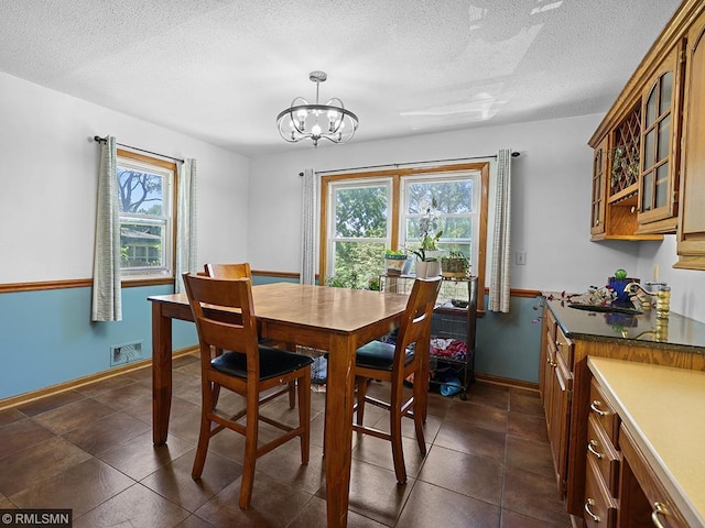 dining area with a textured ceiling, sink, a wealth of natural light, and a chandelier