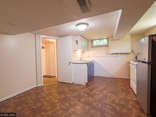 kitchen with sink, dark parquet floors, white range, stainless steel fridge, and white cabinets