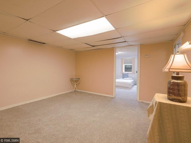 basement featuring a paneled ceiling and light colored carpet