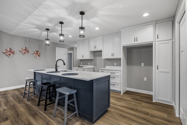 kitchen featuring a center island with sink, white cabinets, hanging light fixtures, and dark hardwood / wood-style floors