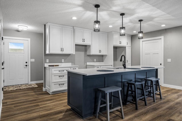 kitchen featuring white cabinetry, dark wood-type flooring, an island with sink, and pendant lighting