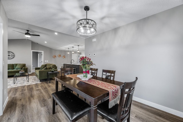 dining space with hardwood / wood-style flooring, ceiling fan with notable chandelier, lofted ceiling, and a textured ceiling