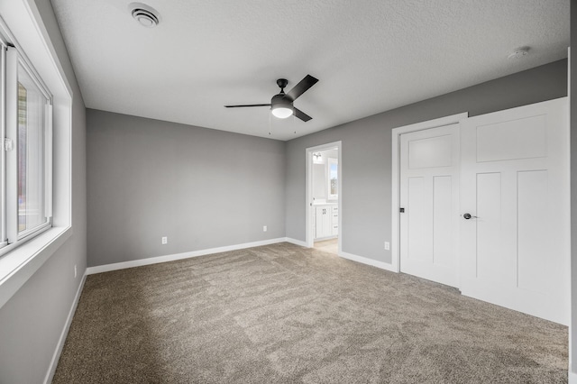 unfurnished bedroom featuring ensuite bathroom, a textured ceiling, ceiling fan, carpet floors, and a closet