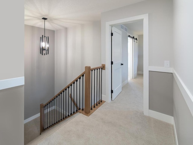 hall with a barn door, light carpet, and an inviting chandelier