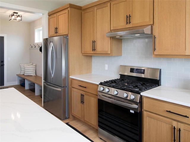 kitchen featuring light stone countertops, light wood-type flooring, stainless steel appliances, and tasteful backsplash