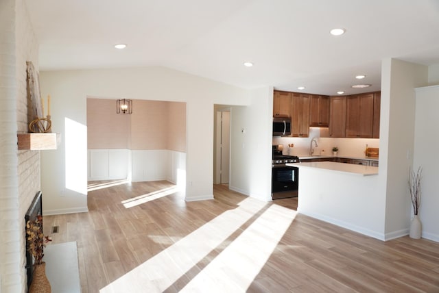 kitchen featuring stainless steel appliances, a fireplace, vaulted ceiling, light hardwood / wood-style flooring, and sink