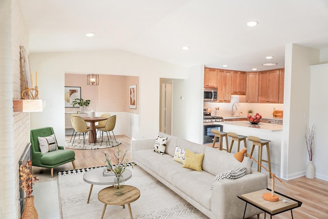 living room featuring light wood-type flooring, vaulted ceiling, a fireplace, and sink