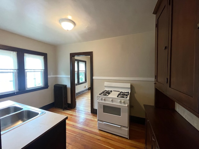 kitchen featuring white range with gas stovetop, sink, radiator heating unit, light hardwood / wood-style flooring, and dark brown cabinetry