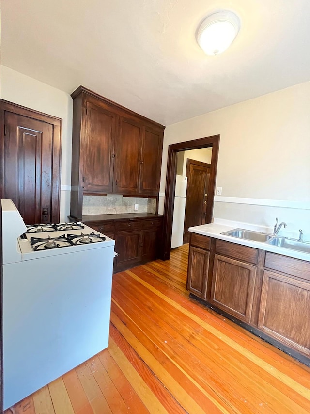 kitchen with decorative backsplash, white appliances, dark brown cabinetry, sink, and light hardwood / wood-style floors