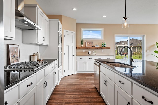 kitchen featuring stainless steel appliances, sink, wall chimney range hood, pendant lighting, and white cabinetry