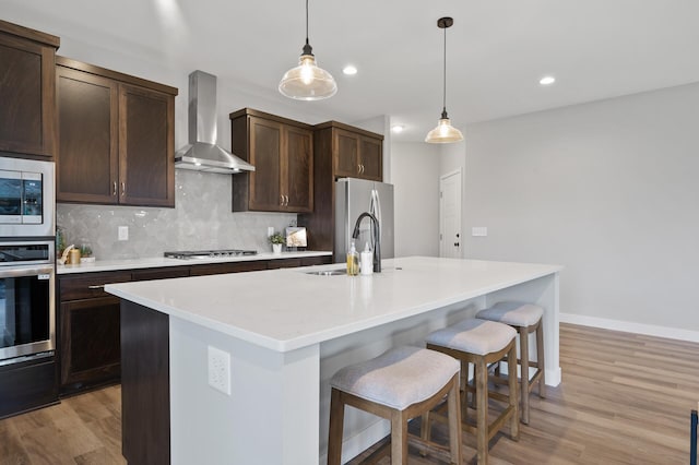 1242 Willowbrook Cir, Delano, MN 55328 - kitchen featuring appliances with stainless steel finishes, wall chimney range hood, light wood-type flooring, decorative backsplash, and a kitchen bar