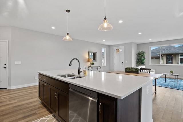 kitchen featuring sink, hanging light fixtures, light hardwood / wood-style flooring, stainless steel dishwasher, and a center island with sink