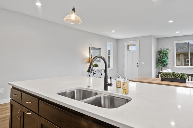 kitchen with sink, light hardwood / wood-style flooring, light stone countertops, decorative light fixtures, and dark brown cabinets