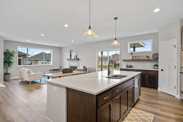 kitchen featuring sink, light hardwood / wood-style flooring, stainless steel dishwasher, an island with sink, and pendant lighting