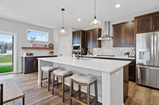 kitchen featuring sink, wall chimney exhaust hood, a kitchen island with sink, decorative backsplash, and appliances with stainless steel finishes