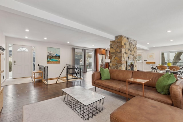 living room with beam ceiling, a stone fireplace, and light wood-type flooring