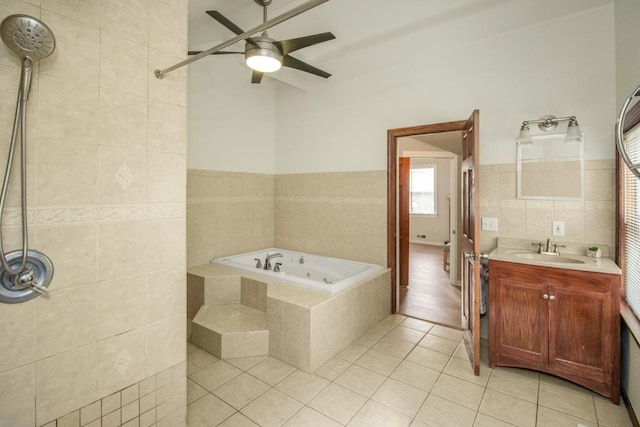 bathroom with tile walls, tile patterned flooring, vanity, ceiling fan, and tiled tub