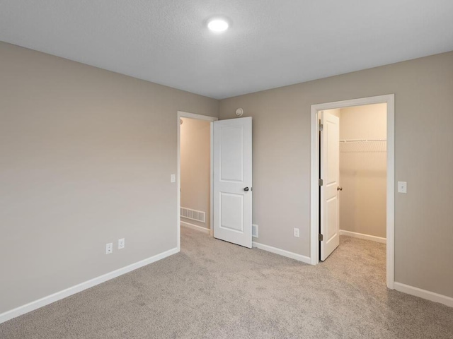 unfurnished bedroom with light colored carpet, a closet, and a walk in closet