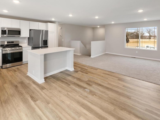 kitchen with appliances with stainless steel finishes, light colored carpet, white cabinetry, and a center island